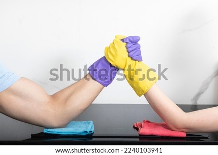 Close up of hands in colourful gloves in arm wrestling position on electric stove with rags. Cleaning service and household concept