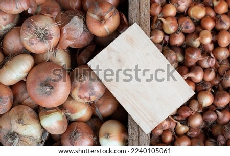 Onions are for sale in various boxes. The bulbs are sorted by size. A blank sign on wood serves as a place for text. The focus is on the wooden shield.