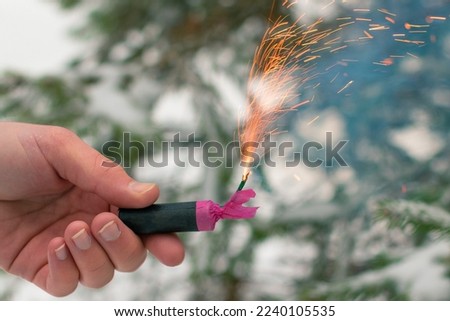 Burning Firecracker in a Hand. Guy Holding a Petard Outdoors in Winter at Daytime. Loud and Dangerous New Year's Entertainment. Hooliganism with Pyrotechnics. Noise of Firecrackers in Public Places Royalty-Free Stock Photo #2240105535