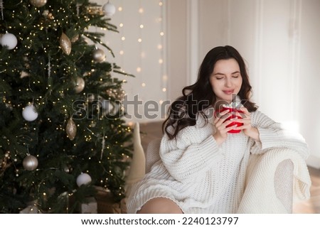 young beautiful  woman wearing a white sweater with a cup of hot Cocoa Drink the Christmas interior  at home.  Enjoying the little things. Winter Vibes. christmas holiday. 