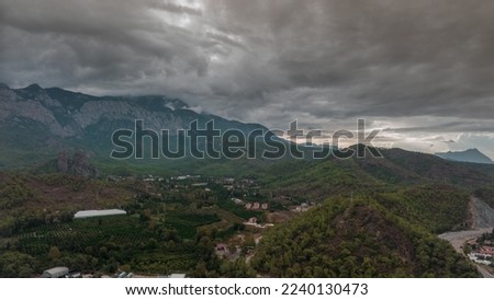 Top view of the hilly green area. Houses in the green forest. Timelapse. Overcast weather. Gray clouds. Photography. High quality photo