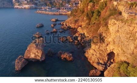  Aerial drone view of rocky shore. Rocks stick out of the water. Old town, pier and ships in the background. Seascape. High quality photo
