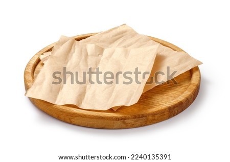 Baking paper on wooden board isolated. Round board with crumpled pieces of brown parchment or baking paper on white background. Design element. Royalty-Free Stock Photo #2240135391