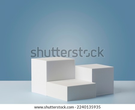 Square podiums are white. Abstract background. A stage for the demonstration of cosmetics. Podium for the award, consisting of three 3 square figures of different sizes on a blue background.  Showcase Royalty-Free Stock Photo #2240135935