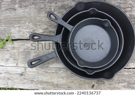 Three cast iron pans placed one inside the other on a wooden table. Cast iron cookware of various sizes used for rustic cuisine cooking. Royalty-Free Stock Photo #2240136737
