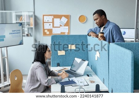 Side view at two young colleagues talking over cubicle wall in office, copy space Royalty-Free Stock Photo #2240141877