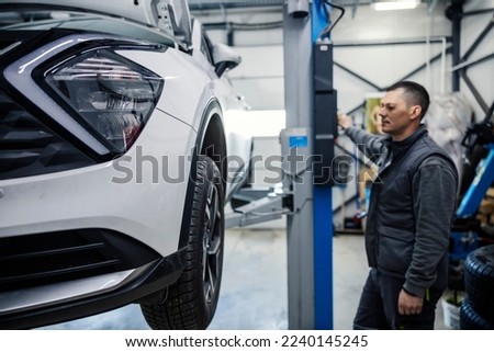 An auto mechanic is lifting car and preparing for maintenance at mechanic's shop. Royalty-Free Stock Photo #2240145245
