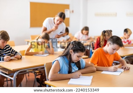 Young girl and boy studying subject in classroom, listening to teacher and writing. Royalty-Free Stock Photo #2240153349