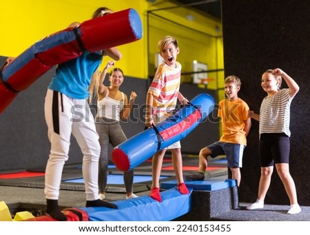 Expressive tween boy having fun on battle beam with his teenage older sisiter over foam pit in indoor trampoline arena..