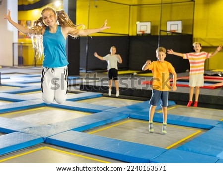 Happy teen girl in blue jersey and white pants jumping and indulging on trampolines in entertainment center Royalty-Free Stock Photo #2240153571