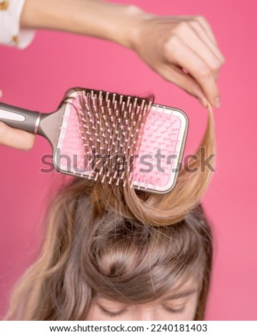 Girl combing her long hair with a comb smiling long curly hair magenta backround