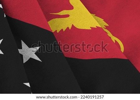 Papua New Guinea flag with big folds waving close up under the studio light indoors. The official symbols and colors in fabric banner