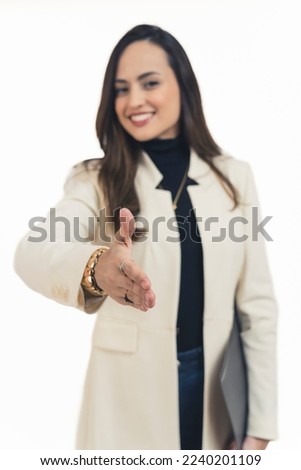 Fashionable latin american businesswoman standing facing camera smiling reaching out to shake hands. Business meeting pov. Focus on foreground. White background vertical studio shot. High quality