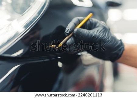 Close up of gloved hand removing small dent from the front of a car in a garage. Car detailing. Horizontal indoor shot . High quality photo