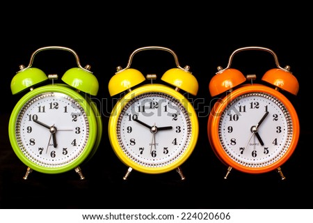 Colorful alarm clocks on black velvet texture  background,  yellow, orange and green. Colorful life style. Daylight Saving Time image.