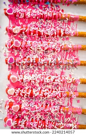 Drizzling melted chocolate over chocolate-dipped pretzels rods and decorating with sprinkles to make chocolate-covered pretzel rods for Valentine's Day.