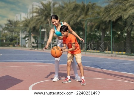 Girl and her younger brother, teenager, play basketball on modern basketball court under open sky.
