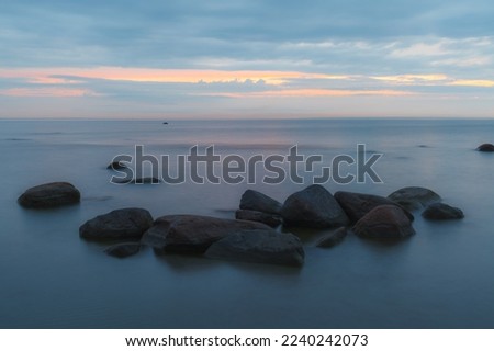 Blue hour after the sunset over rocky Baltic sea cost. Small stones and big boulders in the sea. Long exposure photo.