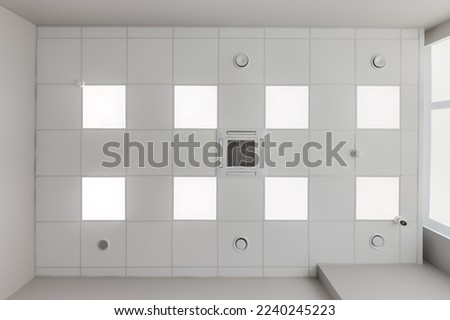 cassette stretched or suspended ceiling with square halogen spots lamps and drywall construction with fire alarm and ventilation in empty room in house or office. Looking up view Royalty-Free Stock Photo #2240245223