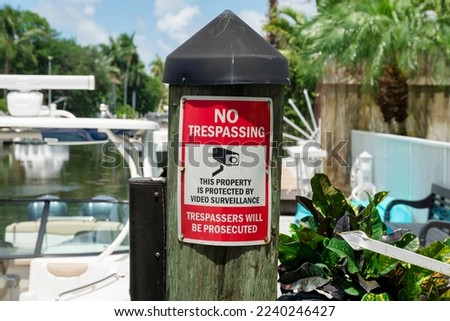 No Trespassing sign on a wood dock post with cap cover at Miami, Florida. Close-up of a warning sign for trespassers with surveillance camera symbol against the boats and wooden wall at the back.