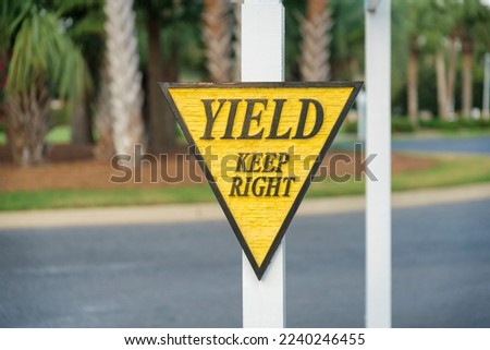 Carved wood road sign with Yield Keep Right at Miami, Florida. close-up of a yield sign on a post with yellow and black frame and letterings against the views of the road and trees.