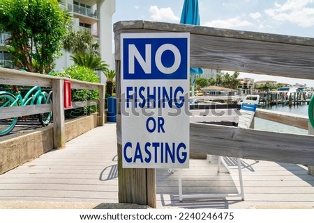 No fishing or casting sign on a wood railings at Destin, Florida. Close-up of a sign against the view of chairs and wooden deck near the water.