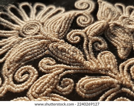 An embroidered bouquet of silk copper-yellow flowers in leaves and curls on a black velvet fabric, in the sun (macro, top view, diagonal, texture).