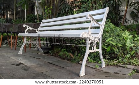 White iron bench in the garden with a decorative ornate metal legs and armrests. Still in usable condition. Picture taken on nice sunny day.