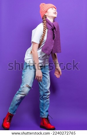 Ful Length Portrait of Caucasian Teenager Girl in Coral Warm Knitted Winter Hat and Violet Scarf Moaning Over Purple Background. Vertical Orientation