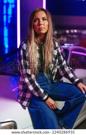 Young beautiful woman with straight long hair posing near white sport car in neon light