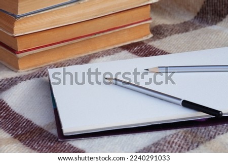 two gray graphite pencils on a sheet of paper with a distinct texture. A sheet on a beige checkered blanket on a background of stack of books