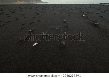 Close up black sand with basalt stones concept photo. Iceland landscape. Front view photography with distant sea on background. High quality picture for wallpaper, travel blog, magazine, article