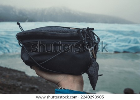 Close up person with camera bag concept photo. First view hand photography with glaciers and mountains on background. High quality picture for wallpaper, travel blog, magazine, article