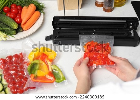 Woman using sealer for vacuum packing with plastic bag of red pepper at white table, closeup Royalty-Free Stock Photo #2240300185