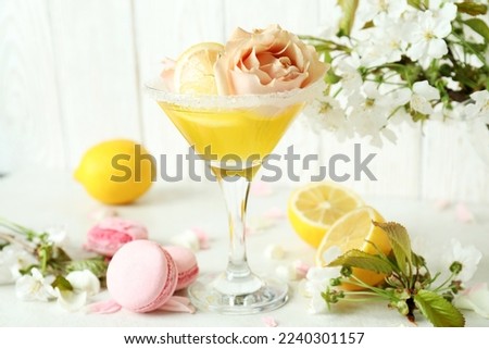 Glass of cocktail, ingredients and flowers on white textured table