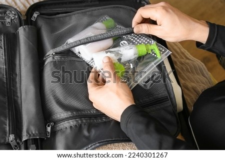 a man collects a suitcase. Puts jars of shampoo and gel in a travel case in a suitcase Royalty-Free Stock Photo #2240301267