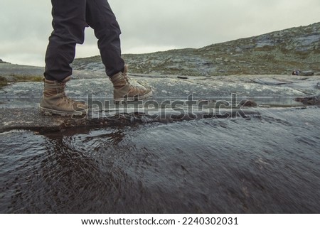 Tourist walking across small mountain river scenic photography. Picture of person with gloomy sky on background. High quality wallpaper. Photo concept for ads, travel blog, magazine, article