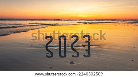 Happy New Year 2023: concept of new year 2023 with a sunrise on the beach and the numbers 2023 reflected in the sea.	