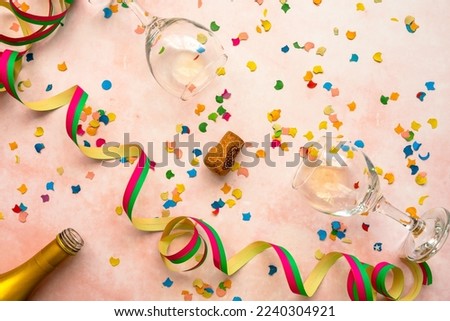 Two lying wine glasses, colorful confetti and streamers on a pink background. Top view, new year.