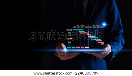 Project manager working on tablet and updating tasks and milestones progress planning with Gantt chart scheduling interface for company on virtual screen. Business Project Management System. Royalty-Free Stock Photo #2240305989