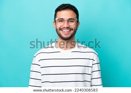 Young Brazilian man isolated on blue background With glasses with happy expression Royalty-Free Stock Photo #2240308583