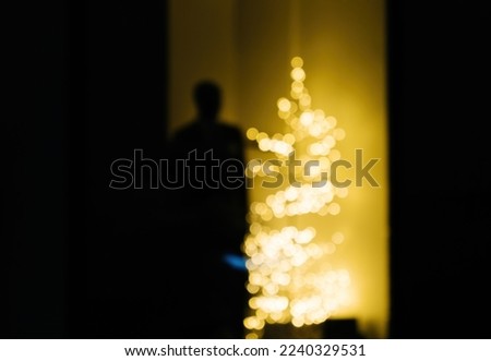 Male silhouette staying near a defocused yellow Christmas fir tree - concept for loneliness during winter holidays, consumerism etc