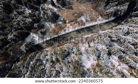 Aerial high angle view of narrow winding curvy mountain road among the trees in winter forest. Snowy landscape, bird's eye view.