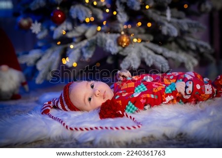 Cute child in Christmas clothes. Baby with lying on the floor. Fur tree at the background. Stock photo