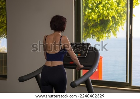 girl trains in gym looking out window at sea. View from back.
