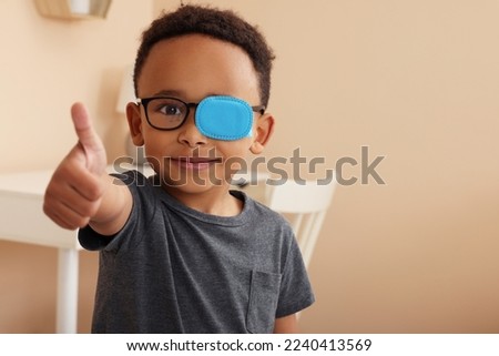 African American boy with eye patch on glasses showing thumb up in room, space for text. Strabismus treatment Royalty-Free Stock Photo #2240413569