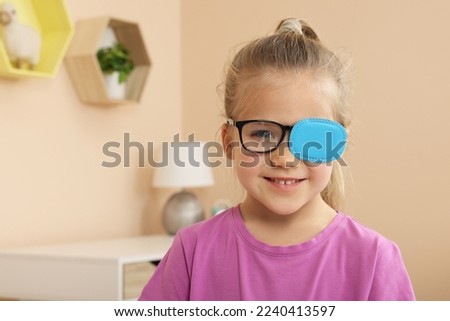 Girl with eye patch on glasses in room, space for text. Strabismus treatment Royalty-Free Stock Photo #2240413597