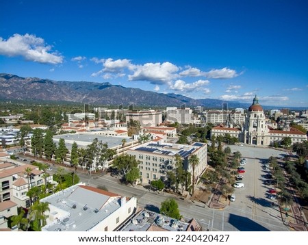 aerial shot of office buildings, city hall and apartments in the city skyline surrounded by lush green trees and plants, cars on the street, mountains, blue sky and clouds in Pasadena California Royalty-Free Stock Photo #2240420427