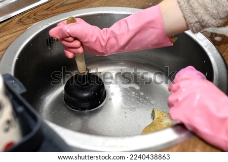 woman's hands with a plunger unclogging the kitchen drain because it is clogged with leftover food. need plumber Royalty-Free Stock Photo #2240438863