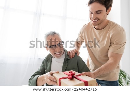 young man giving gift box to happy dad while congratulating him on fathers day